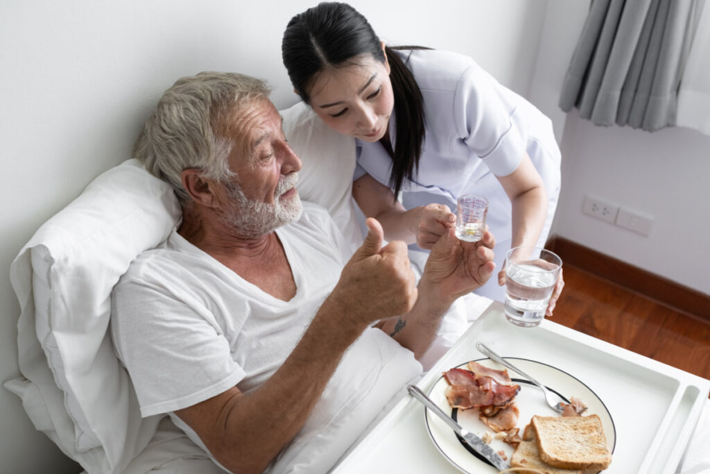 nurse give pill to senior man after breakfast and discussion on bed at nursing home