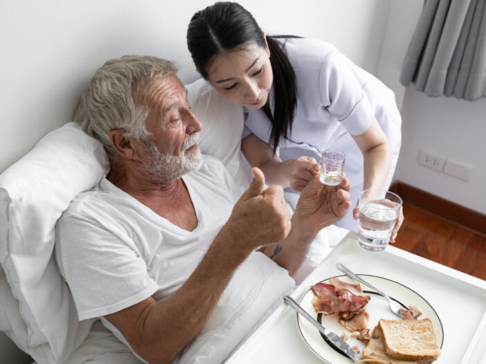 nurse give pill to senior man after breakfast and discussion on bed at nursing home